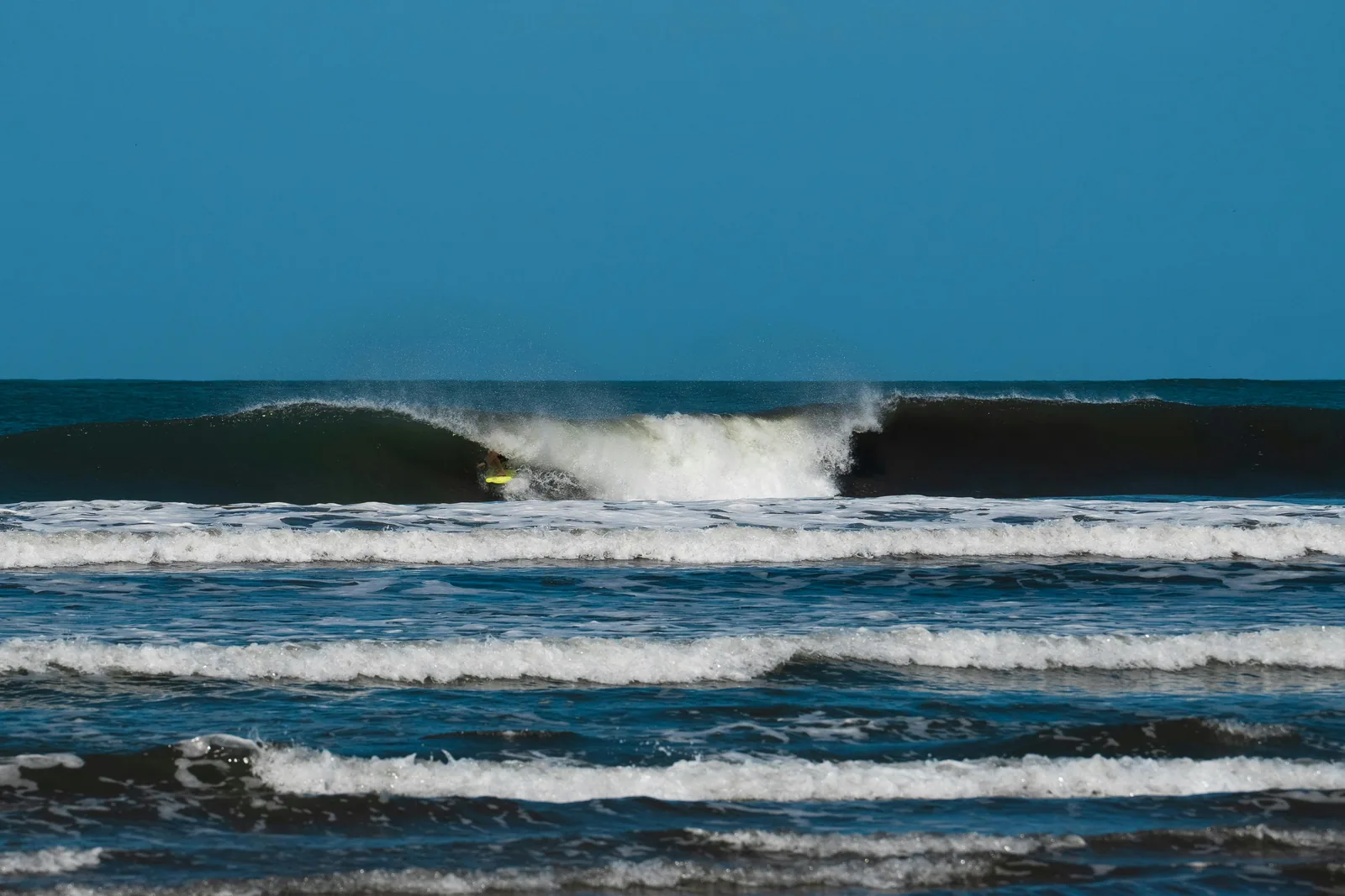 An offshore wind feathering the lip of a clean A-frame peak. This is the shape a good sandbar makes when the wind lines up behind the swell.